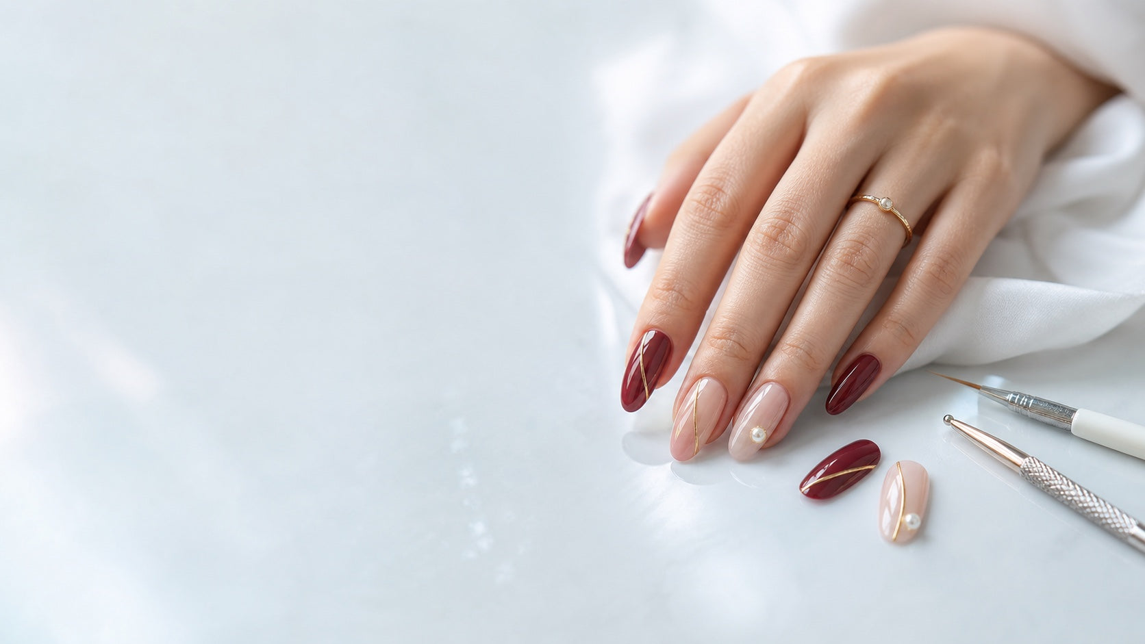 A bespoke burgundy and nude press-on nail set with fine gold details